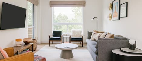 Un salón moderno con un sofá gris, una mesita redonda y un televisor montado en la pared.