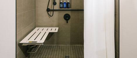 A shower stall with a white shower curtain, a handheld showerhead, a handheld shower head, and a shelf with toiletries.