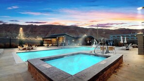 A pool area with lounge chairs and a hot tub, surrounded by a building with a mountain backdrop.