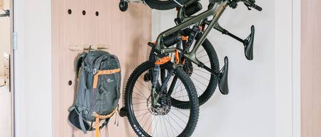 A room with a wooden wall-mounted bike rack holding two bicycles and a backpack.