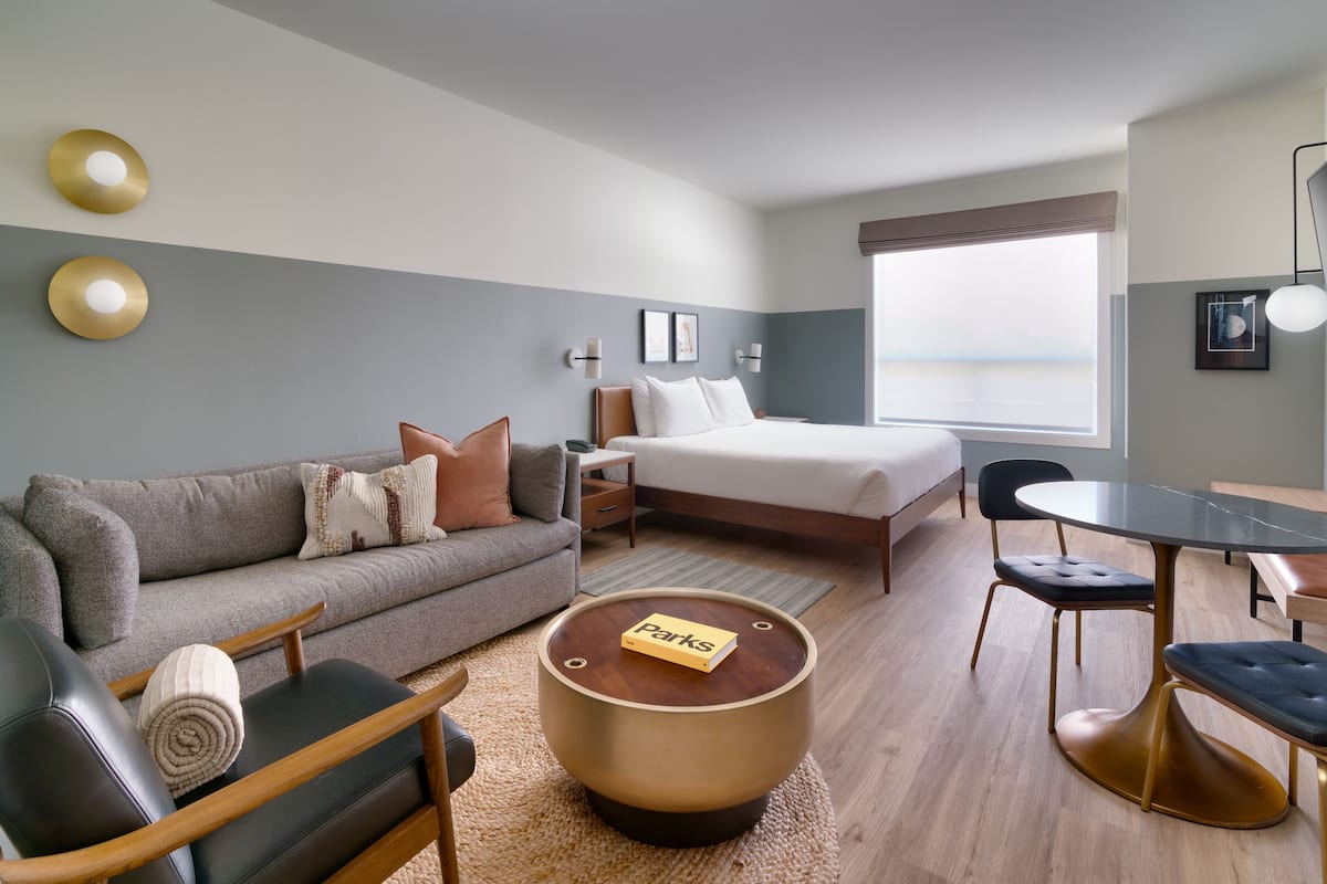 A modern hotel room with a bed, a sofa, a dining table, and a TV.