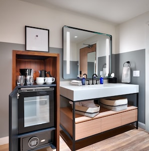 A modern bathroom with a built-in coffee machine, a large mirror, and a vanity with storage baskets.