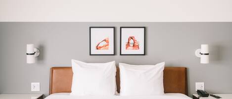 A hotel room with a large bed, two bedside tables, a nightstand, and two framed pictures on the wall.