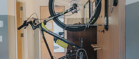 A room with a bicycle mounted on a wall, a wooden floor, and a door leading to another room.
