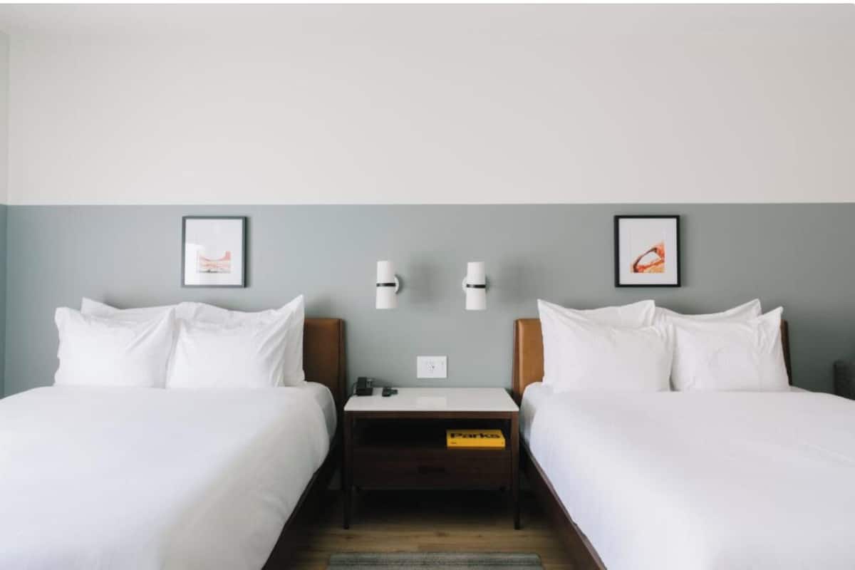 A hotel room with two beds, a nightstand, and two wall-mounted lamps.