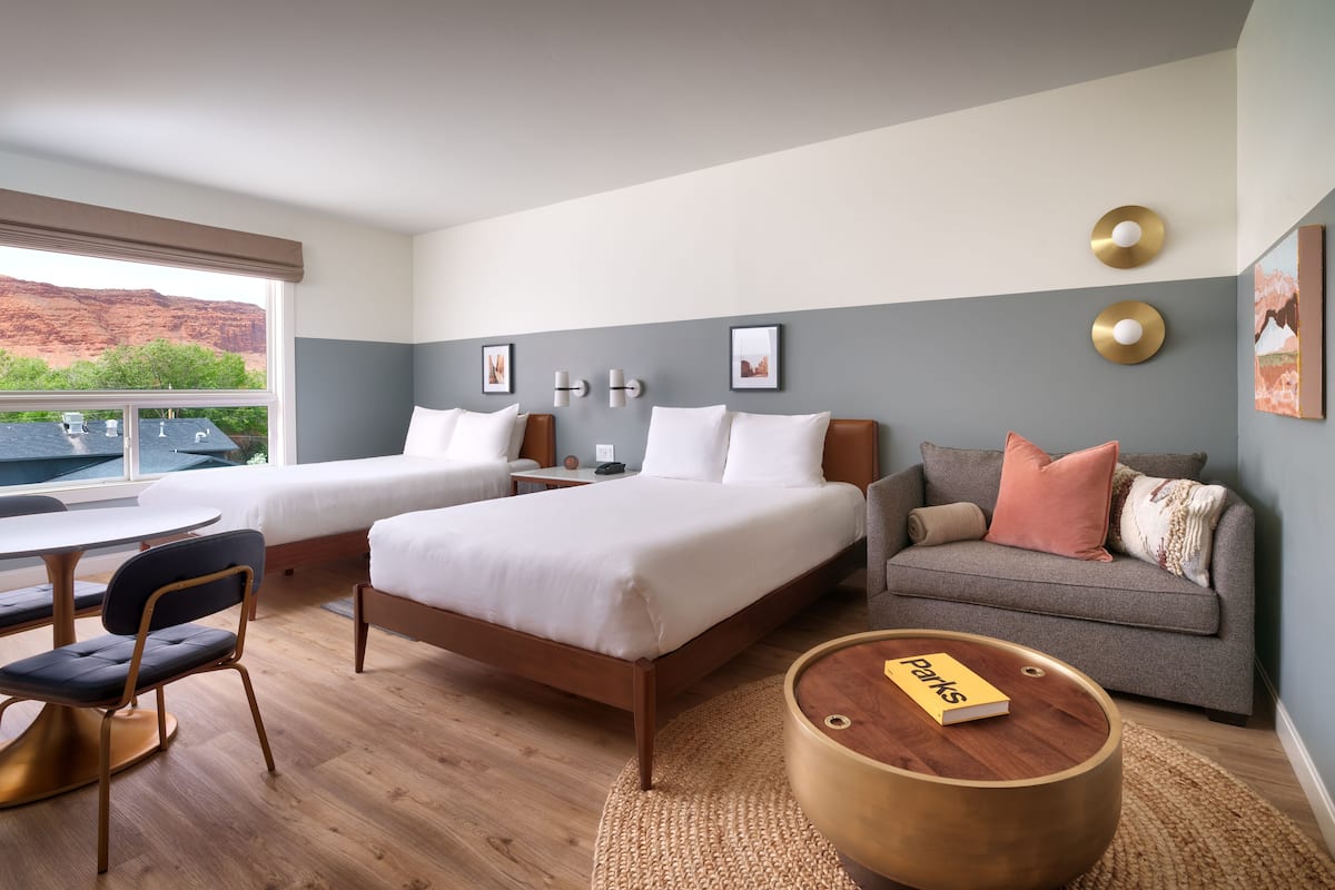 A hotel room with two beds, a sofa, a dining table with chairs, and a view of the outdoors.