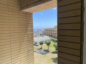 Vista desde una ventana con un muro de diseño cuadriculado, que da a un patio con un parque infantil y edificios al fondo.
