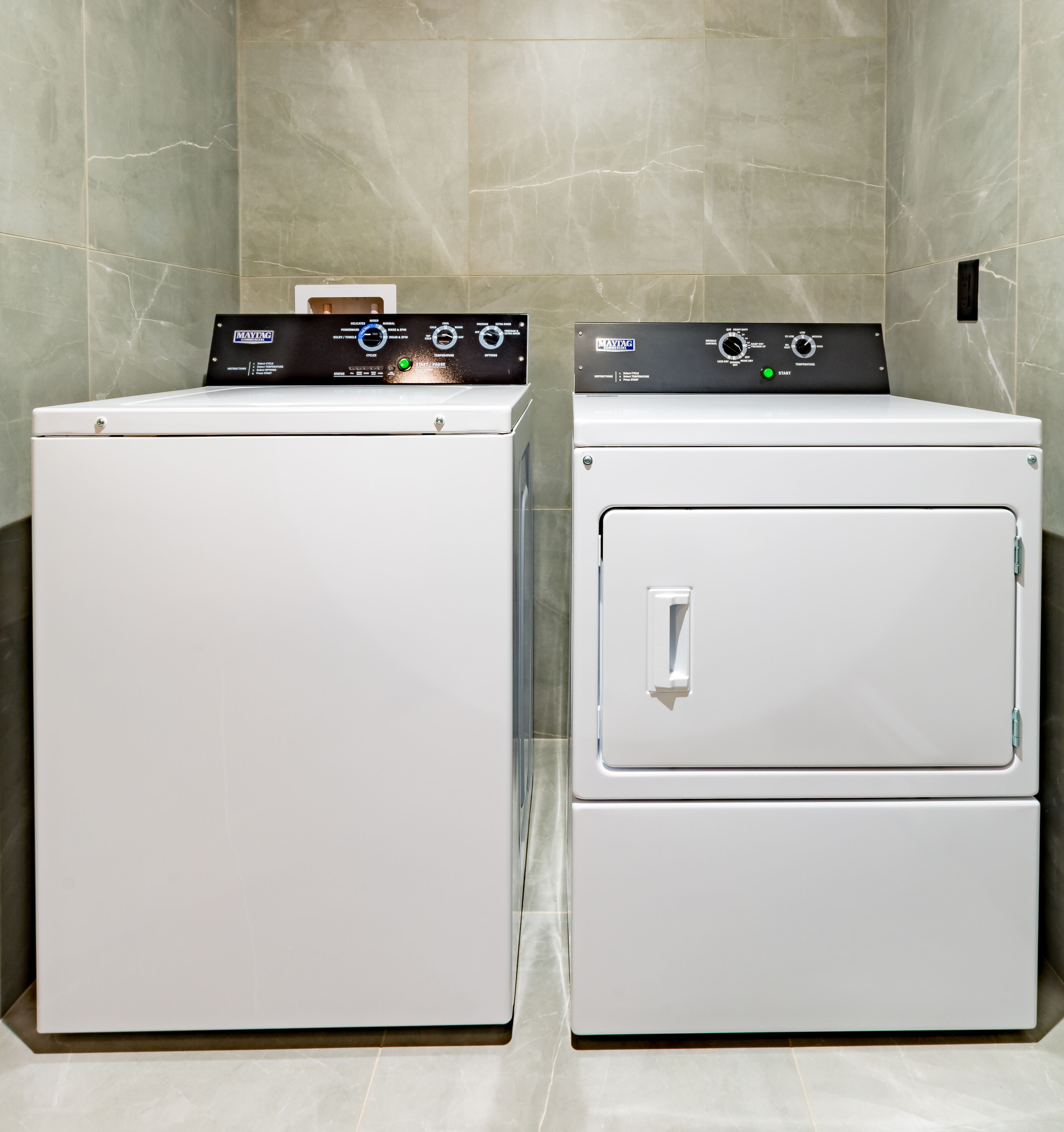 Deux machines à laver à chargement frontal, superposées, dans une salle de bain aux murs en marbre.
