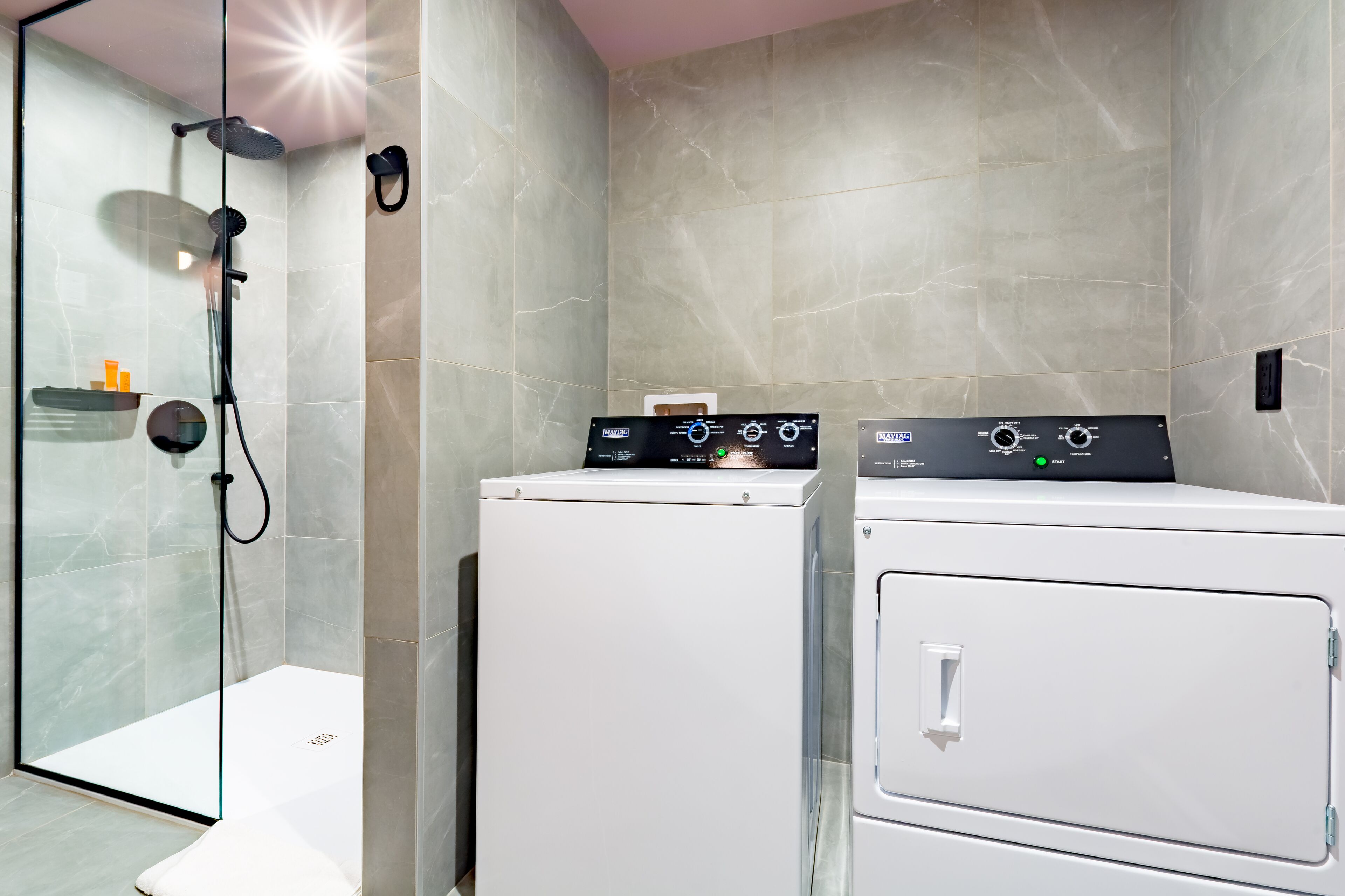 A modern bathroom with a glass-enclosed shower, a washing machine, and a dryer.