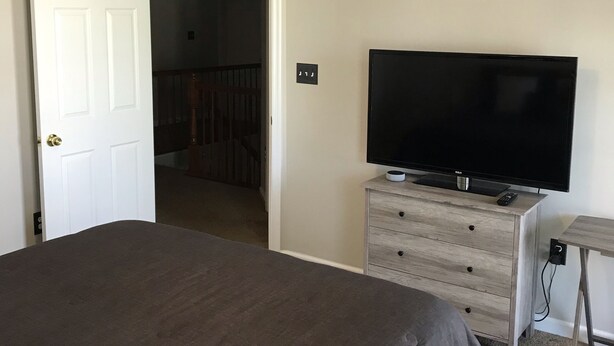 A bedroom with a bed, a ceiling fan, a TV on a dresser, and a door leading to another room. - Simple Serenity  (Fredericksburg)