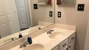 A bathroom with two sinks, a toilet, and a mirror. There are two towel racks and a towel rack with a towel. - Simple Serenity  (Fredericksburg)