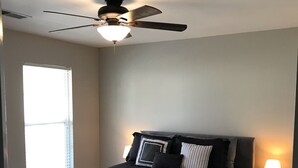 A bedroom with a bed, a ceiling fan, a nightstand, and a window. - Simple Serenity  (Fredericksburg)