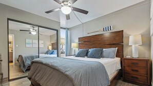 Een slaapkamer met een groot bed, een houten nachtkastje, een plafondventilator en een spiegel.