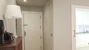 A hallway with a closed door, a lamp, and a kitchen area visible through an open door.