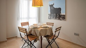 A dining area with a round table, four wooden chairs, a hanging light fixture, and a bull painting on the wall.