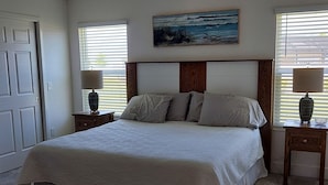 Een slaapkamer met een groot bed, twee nachtkastjes, een plafondventilator, een schilderij aan de muur en een deur.