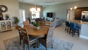 Een ruime woonkamer met een eettafel, stoelen en een keuken met een koelkast en barstoelen.