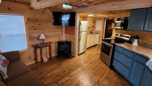 Une chambre confortable, aménagée dans le style d’un chalet, avec un intérieur en bois, un canapé, une petite table avec une lampe, un téléviseur et un coin cuisine équipé d’un réfrigérateur, d’une cuisinière et de placards.