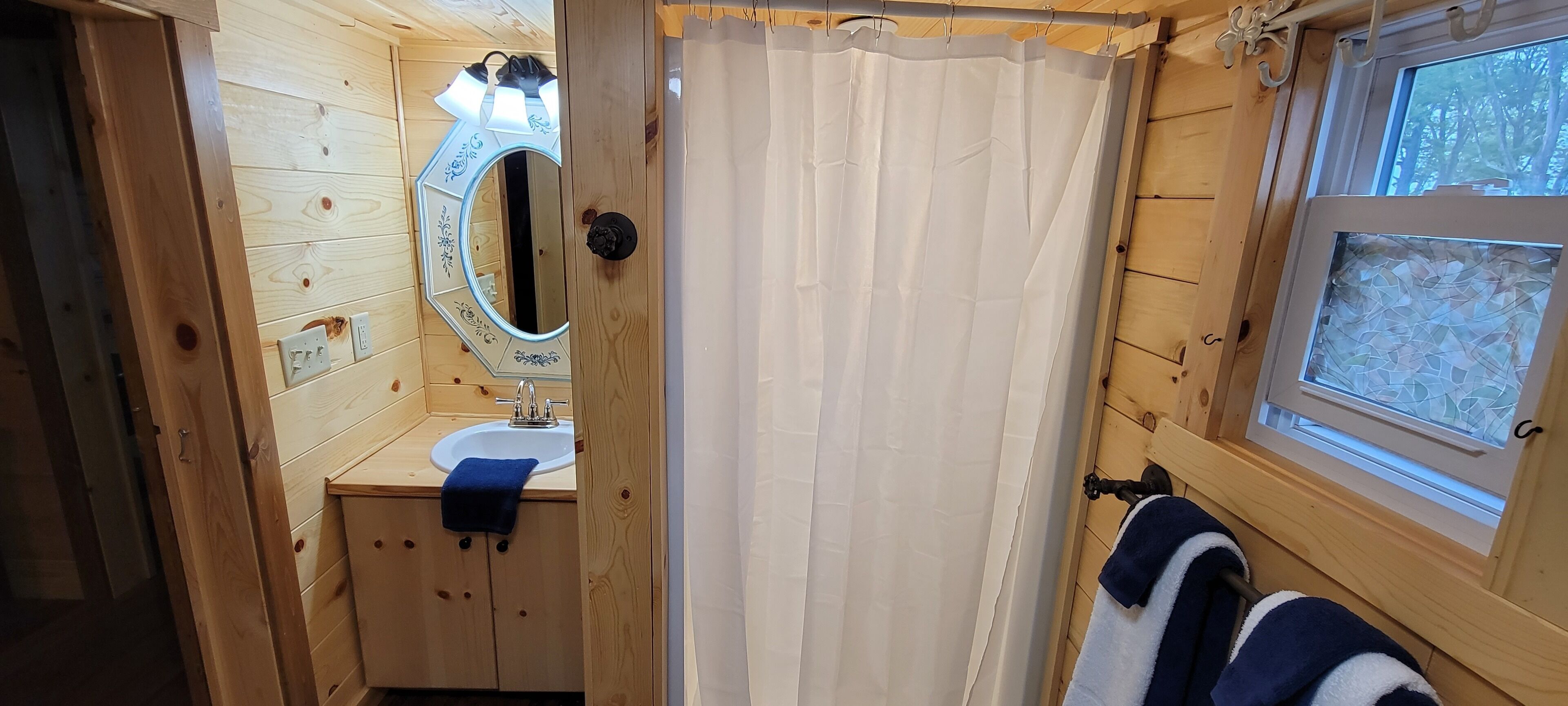 A wooden cabin bathroom with a sink, mirror, and window.