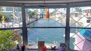 Vista desde una ventana sobre un puerto deportivo con barcos, un paisaje tropical y un lagarto decorativo.