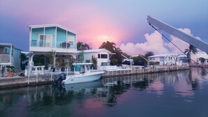 Una propiedad frente al mar con un barco amarrado, un muelle que se adentra en el agua y un atardecer al fondo.