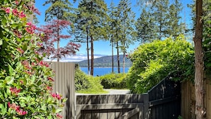 En träport som leder in till en frodig trädgård med utsikt över en sjö och berg.
