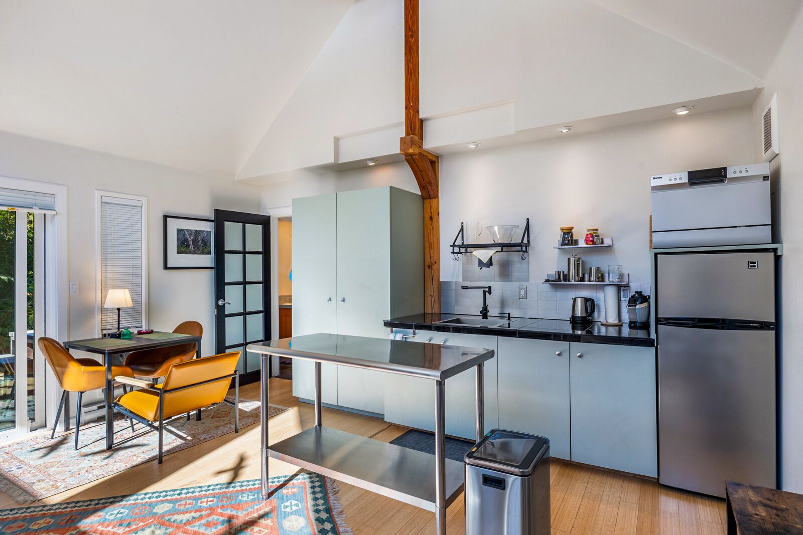 A modern kitchen with a dining area, featuring a large window, a built-in oven, and a refrigerator.