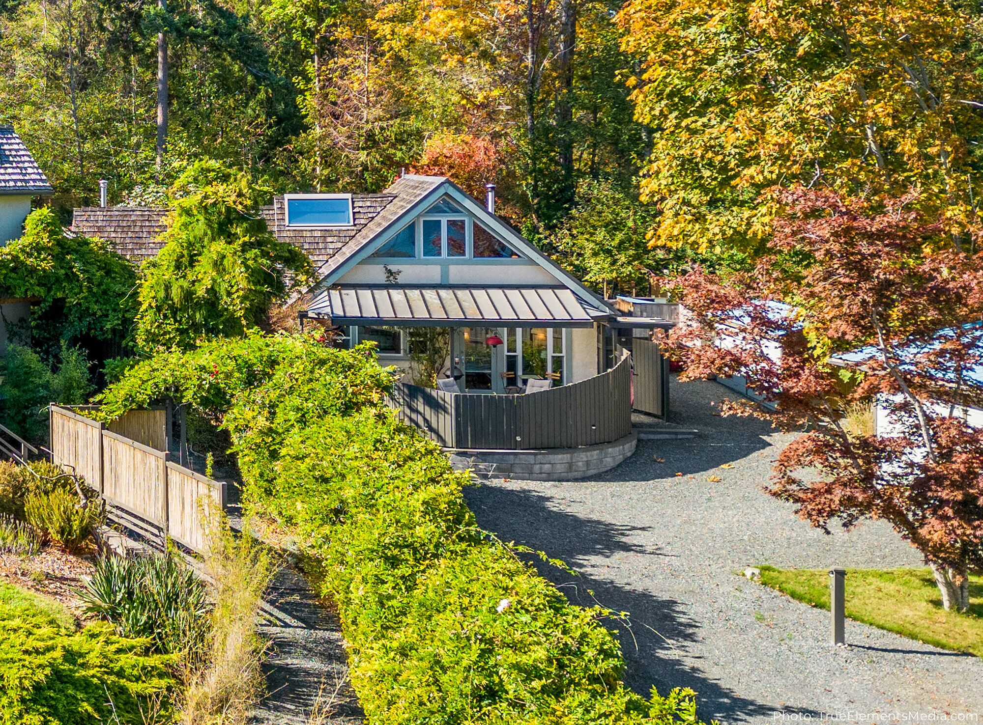 A house with a covered porch, surrounded by trees and a gravel driveway.