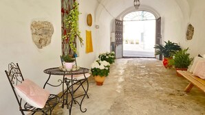A corridor with a round table and chairs, potted plants, and a bench. - [Arcada 4] Apartment in the heart of Orosei (Orosei)