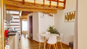 A modern kitchen with wooden beams, a dining area with white chairs, and a potted plant. - [Arcada 4] Apartment in the heart of Orosei (Orosei)
