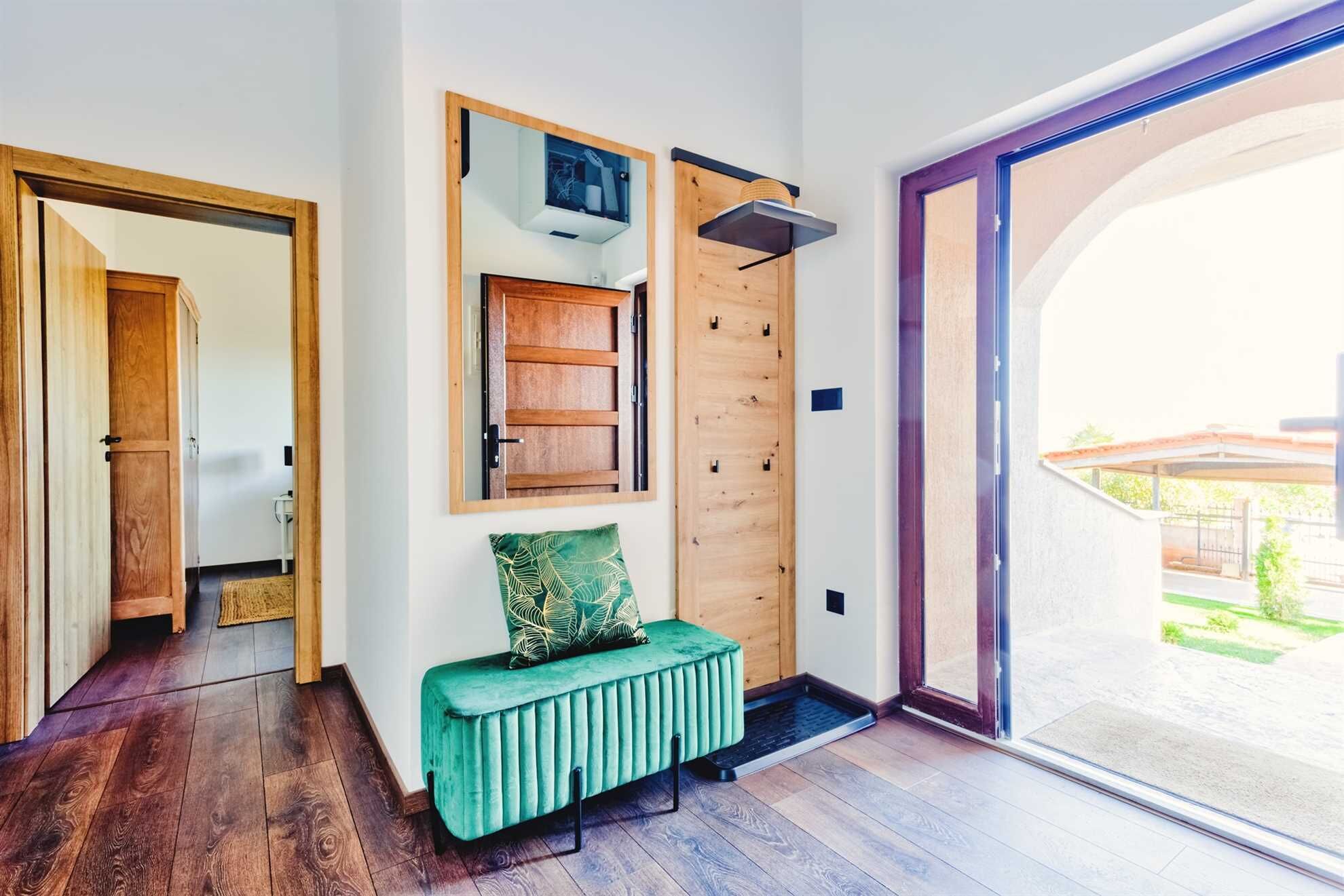 A modern interior with a wooden door, a green bench, and a view through a glass door.