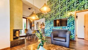 Een moderne hotel lobby met een muur met een bladpatroon, een flatscreen televisie, een grijze bank en een marmeren salontafel met een bloevas.