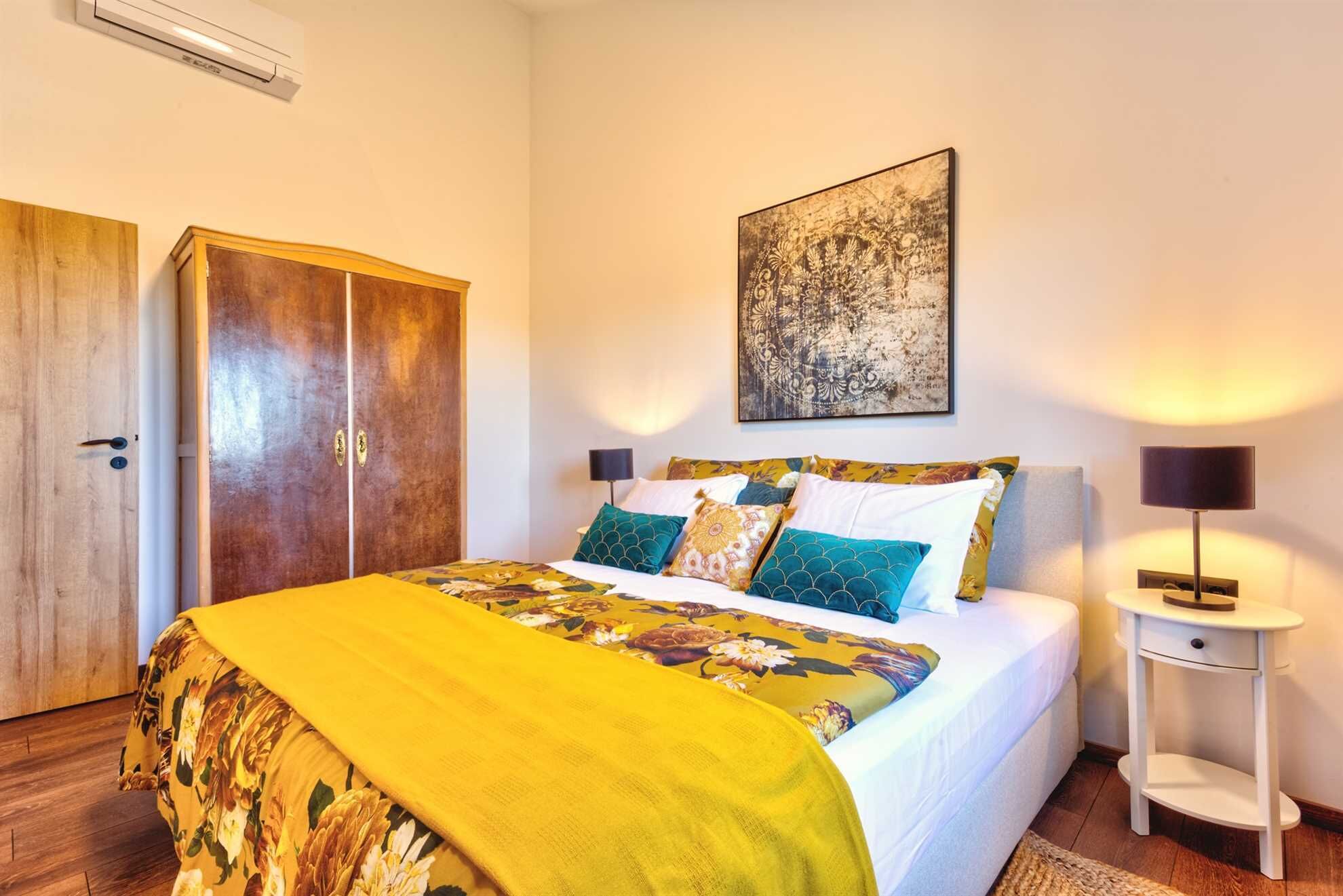 A bedroom with a bed, a wardrobe, a bedside table, and a wall-mounted artwork.