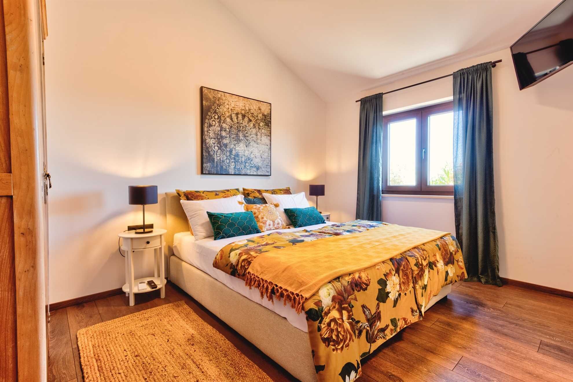 Una camera da letto con un letto, un comodino, una lampada, un quadro appeso e una finestra con tende.