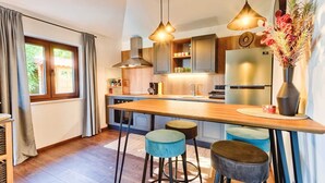 Een moderne keuken met houten aanrechtbladen, een centraal eiland, barkrukken, hanglampen en een koelkast.