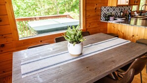 A wooden dining table with a striped placemat, a potted plant, and a view of a wooden deck and greenery outside. - Well-appointed cabin with expansive mountain views, nature and tranquility. (Zionville)
