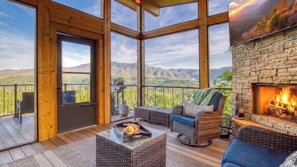 A spacious balcony with a stone fireplace, wicker furniture, and a scenic mountain view.
