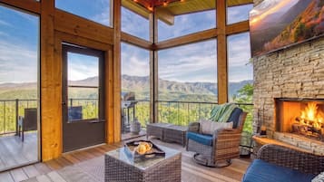 A spacious balcony with a stone fireplace, wicker furniture, and a scenic mountain view.