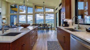 A modern kitchen with a large island, wooden cabinets, and a view of the mountains.