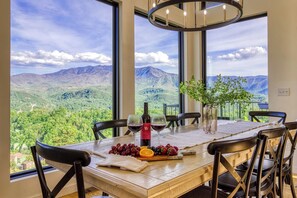 A dining table with a view of mountains, a bottle of wine, and a vase with a plant. - Minutes from Downtown Gatlinburg~Sleeps 12/5Baths ~ Stunning Views~ Hot Tub~Pool (Gatlinburg)