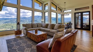 A spacious living room with a large sectional sofa, a wooden coffee table, and a view of mountains through large windows.