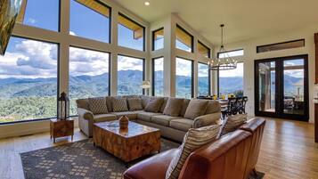 A spacious living room with a large sectional sofa, a wooden coffee table, and a view of mountains through large windows.