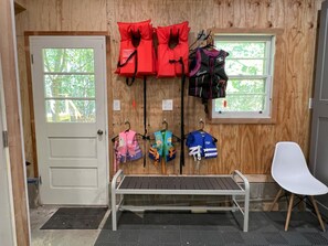 A room with a white door, a bench, and a white chair. There are life jackets and jackets hanging on the wall. - Lakefront Retreat, Renovated, Pet Friendly, Close to All Area Attractions (Pocono Summit)