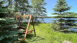 A wooden swing set in a grassy area with a lake and trees in the background. - Lakefront Retreat, Renovated, Pet Friendly, Close to All Area Attractions (Pocono Summit)