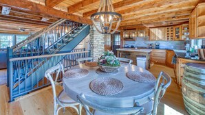 L’intérieur d’un chalet rustique est agrémenté d’un escalier en bois, d’une table de salle à manger ronde avec des sets de table, et d’un coin cuisine.