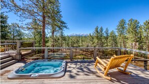 Un bain à remous sur une terrasse en bois, avec vue sur une forêt et des montagnes en arrière-plan.