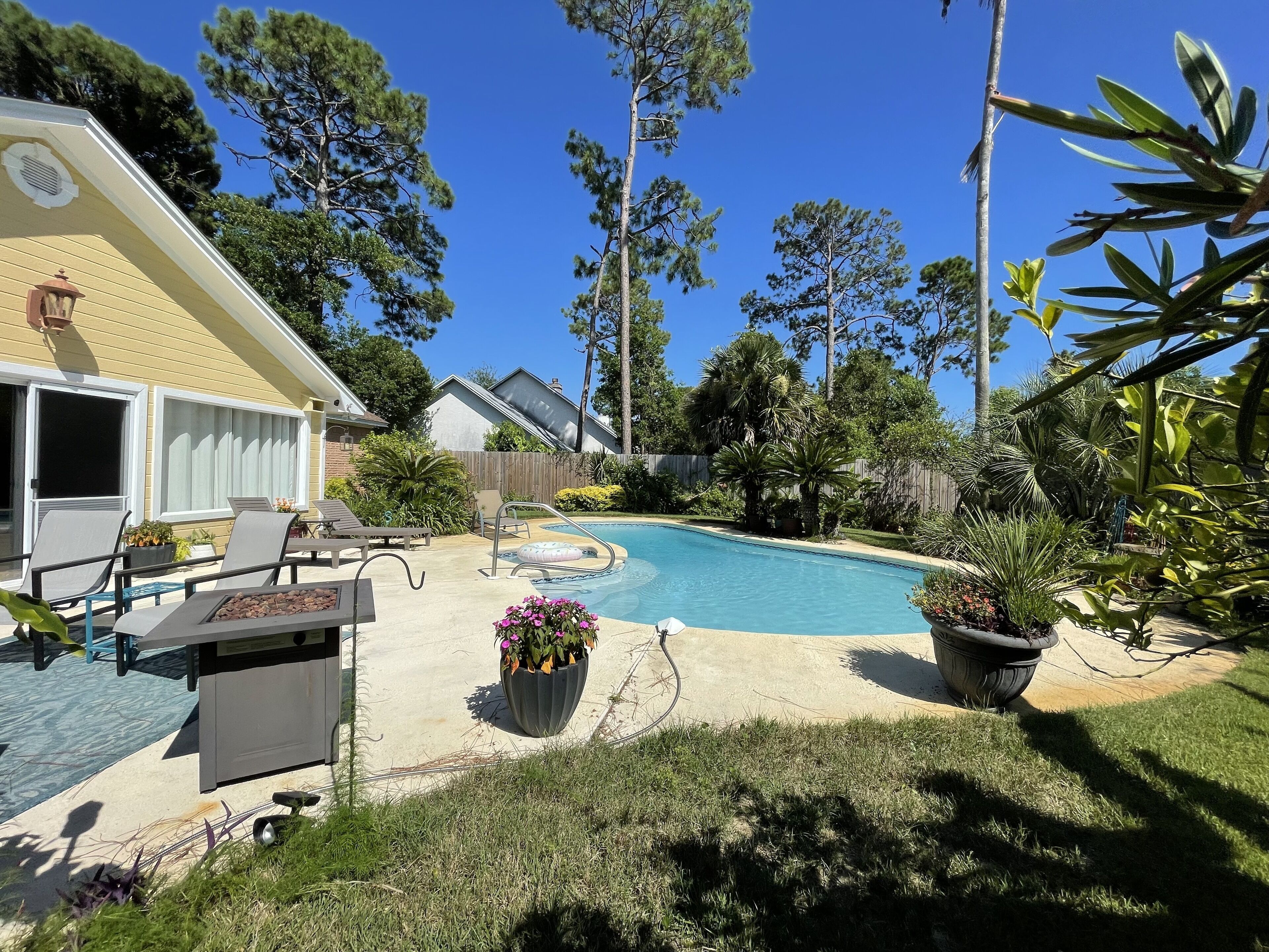 Un patio trasero con piscina, mobiliario exterior y diversas plantas.