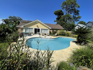 Ein Garten mit Swimmingpool, einer überdachten Terrasse und einem Haus mit gelber Fassade.