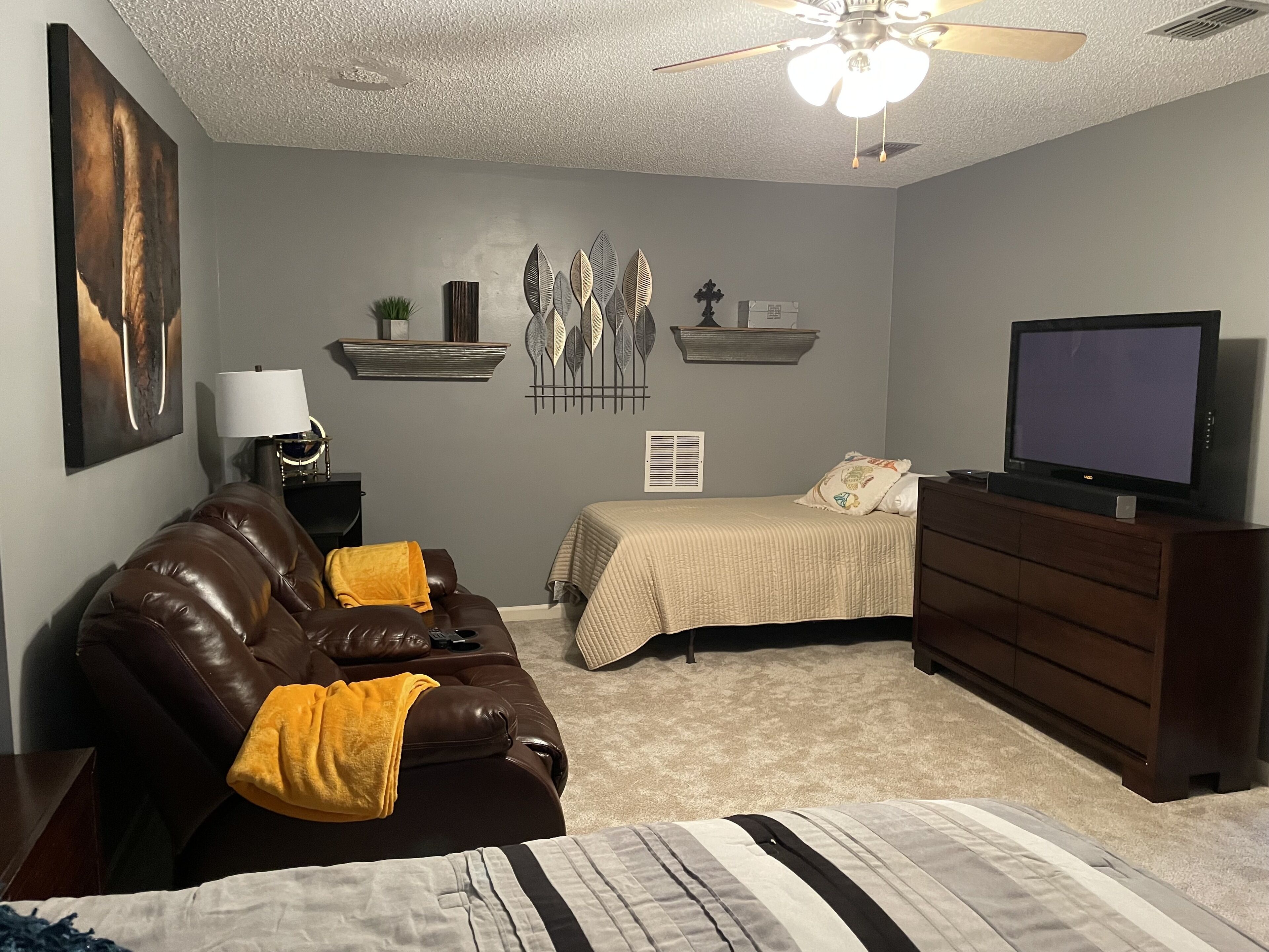 Um quarto com cama, sofá de couro, televisão e ventilador de teto.