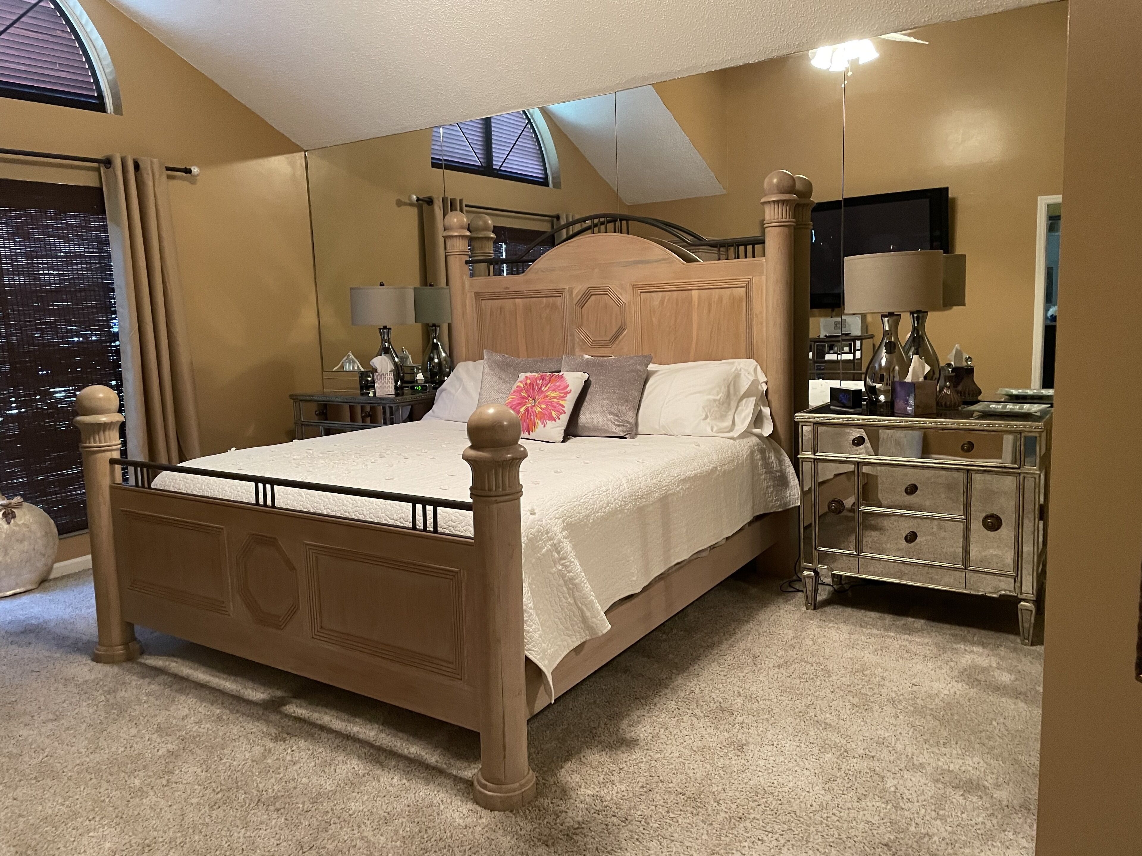 Een slaapkamer met een groot bed, een nachtkastje, een spiegel en een raam met uitzicht op de stad.